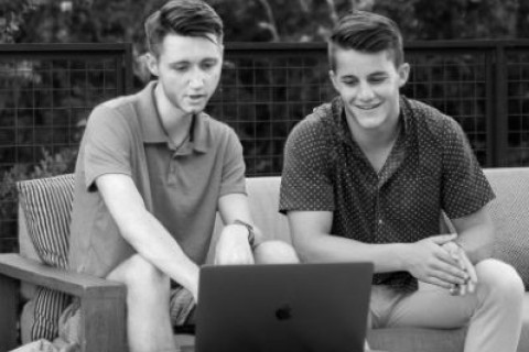 zwei Jugendliche diskutieren vor dem Laptop.
