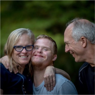 Erziehungsauftrag-Mutter Vater und Sohn mit Downsyndrom lachen gemeinsam.