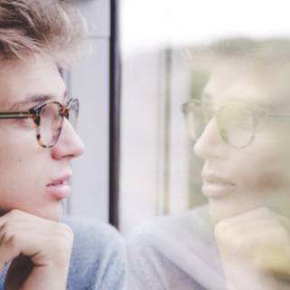 Jugendlicher schaut aus dem Zugfenster und sieht sein Spiegelbild